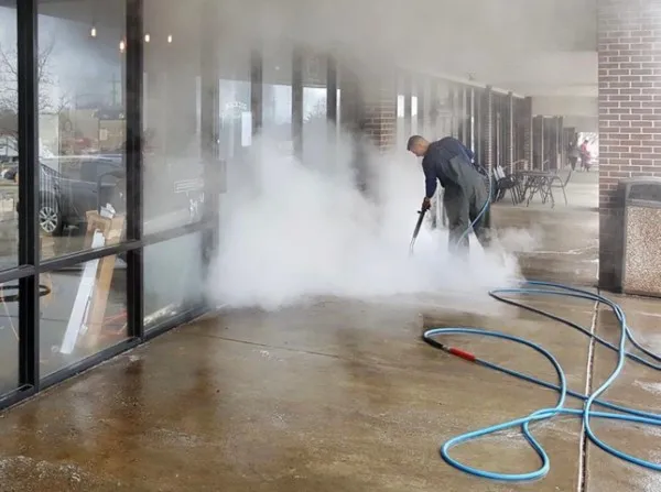Man pressure washing building's sidewalk entrance.